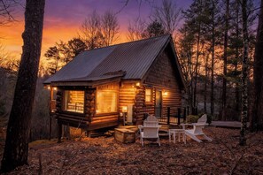 Une cabane en rondins avec un porche, deux fauteuils Adirondack et un banc en bois.