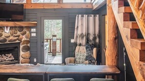A rustic cabin interior with a stone fireplace, wooden ceiling, and a bar area with green bar stools. - Hot Tub, Views, & True Smoky Mountain Charm! (Sevierville)