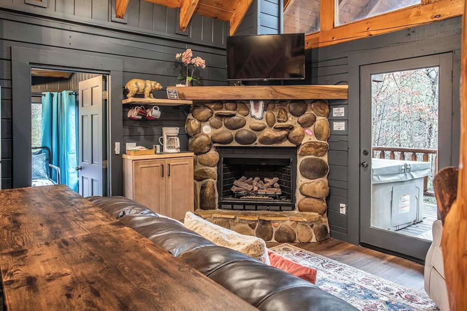 Un acogedor interior de cabaña con chimenea de piedra, muebles de madera y un televisor montado encima.