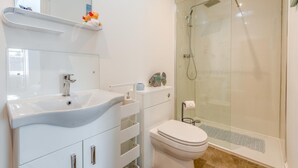 A modern bathroom with a white sink, mirror, and toilet, a glass shower enclosure, and a small shelf with decorative items. - 1 Bed in Gilsland (oc-h32687) (Waterhead)