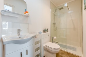 A modern bathroom with a white sink, mirror, and toilet, a glass shower enclosure, and a small shelf with decorative items. - 1 Bed in Gilsland (oc-h32687) (Waterhead)