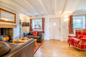 Ein gemütliches Wohnzimmer mit Kamin, Ledersofas, einem roten Karo-Sessel und Holzboden.