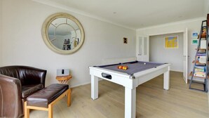 Ein Zimmer mit Poolbillard, einem braunen Ledersofa, einem Holztisch und einem Spiegel an der Wand.