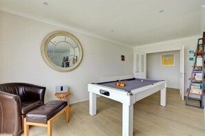 Ein Zimmer mit Poolbillard, einem braunen Ledersofa, einem Holztisch und einem Spiegel an der Wand.