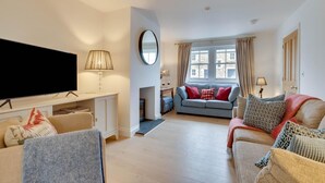 A living room with a flat-screen TV, a fireplace, a sofa, and a dining area with a table and chairs. - 4 Bed in Ellingham (oc-gd1929) (Ellingham)