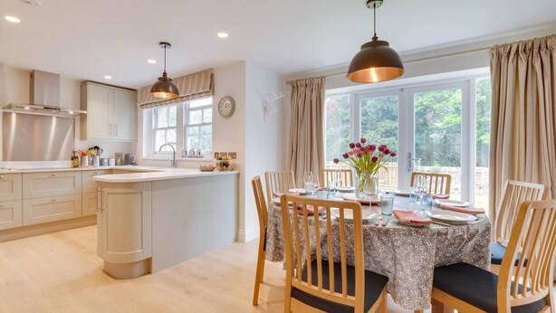 A modern kitchen with a central island, wooden chairs, and a dining table set for four. - 4 Bed in Ellingham (oc-gd1929) (Ellingham)