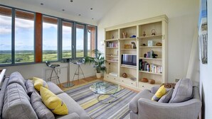 Een moderne woonkamer met een groot raam, een boekenkast en een bank.