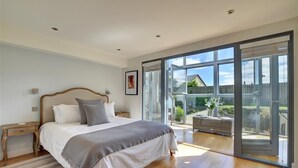 Een slaapkamer met een groot bed, een nachtkastje en een glazen schuifdeur naar een balkon met buitenmeubilair.