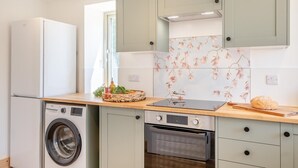 Eine kompakte Küche mit Waschmaschine, Backofen und einer Holzausziehtafel mit einer Korb voller Gemüse.
