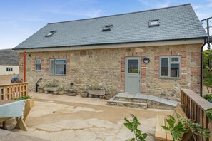 Ein Steinhaus mit grauem Dach, einer Haustür und einer kleinen Veranda mit Topfpflanzen.