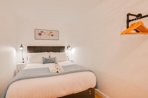 A neatly made bed with pillows, a bedside table with a lamp, and a wall-mounted rack with clothes. - 1 Bed in Langland (oc-hh1425) (Newton)