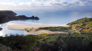 Un paisaje costero con una playa de arena, colinas cubiertas de hierba y una vista despejada del mar.