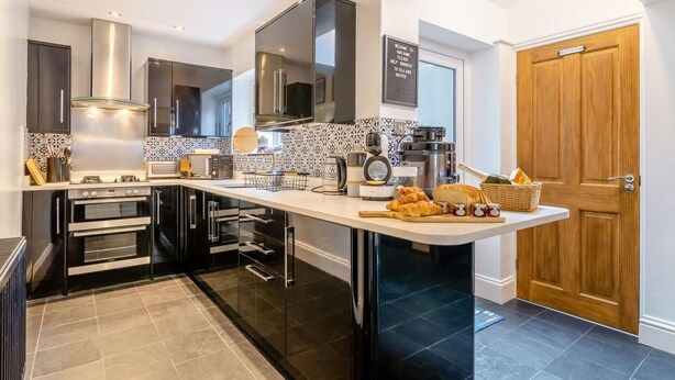 A modern kitchen with stainless steel appliances, a central island, and a wooden door labeled 'bathroom'. - 3 Bed in Whitby (oc-w1018) (Whitby)