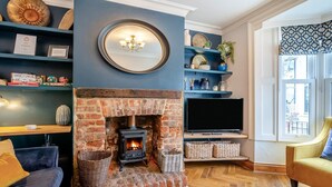 A living room with a brick fireplace, a television, and a sofa. - 3 Bed in Whitby (oc-w1018) (Whitby)