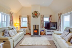 A cozy living room with two sofas, a fireplace, a TV, and large windows. - 3 Bed in Isle Of Skye (oc-s32340) (Glenhinnisdal)