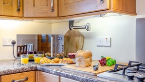 A kitchen with wooden cabinets, a marble countertop, a toaster, a cutting board with bread and fruit, and a stove. - 3 Bed in Isle Of Skye (oc-s32340) (Glenhinnisdal)