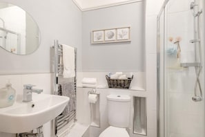 A modern bathroom with a sink, toilet, and shower. There is a mirror, towel rack, and a basket with toiletries. - 6 Bed in Bacton (oc-2187) (Bacton)