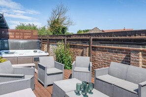 Une terrasse dotée de meubles en osier, d’un jacuzzi et d’un mur en briques.