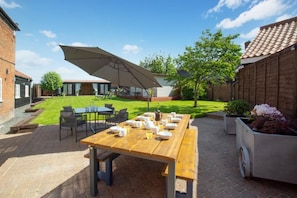A patio with a wooden table set for breakfast, outdoor seating, and a large umbrella. - 6 Bed in Bacton (oc-2187) (Bacton)