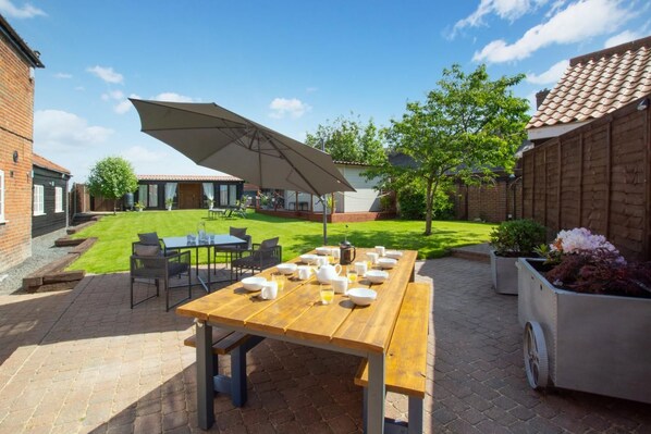 Une terrasse avec une table en bois mise pour le petit-déjeuner, des sièges d’extérieur et un grand parasol.