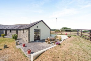 A stone building with a white exterior, a wooden fence, and a patio area with a table and chairs. - 3 Bed in St Columb (oc-trembl) (Saint Mawgan)