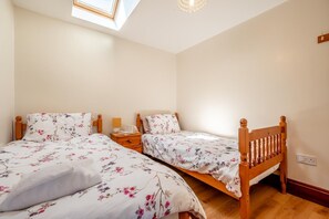 Ein Schlafzimmer mit zwei Einzelbetten, einem Holzkopfstück, einem Nachttisch mit Lampe und einer Steckdose an der Wand.