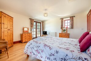 A bedroom with a large bed, wooden wardrobe, and a television. - 3 Bed in St Columb (oc-trembl) (Saint Mawgan)