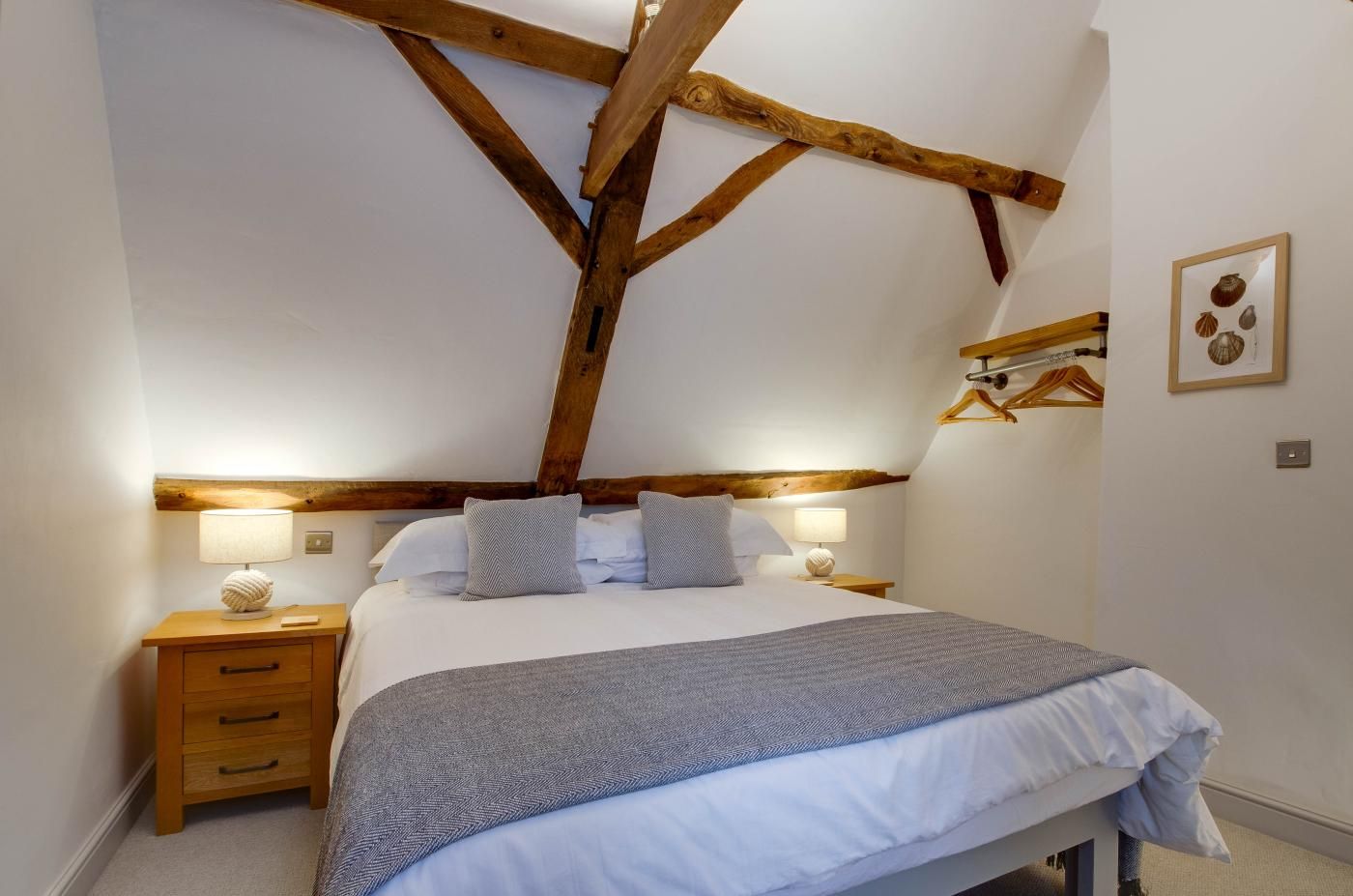 A bedroom with a wooden ceiling, a bed with white bedding, two bedside tables with lamps, and a wall-mounted coat rack.