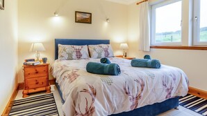 Une chambre à coucher avec un lit, deux tables de chevet, une horloge, une lampe, une fenêtre avec des rideaux et un tableau au mur.
