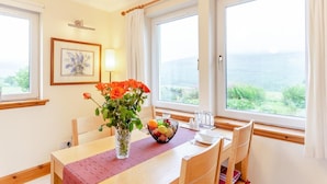 Un coin repas avec une table en bois, des chaises, un vase de fleurs, un panier de fruits et un tableau encadré au mur.