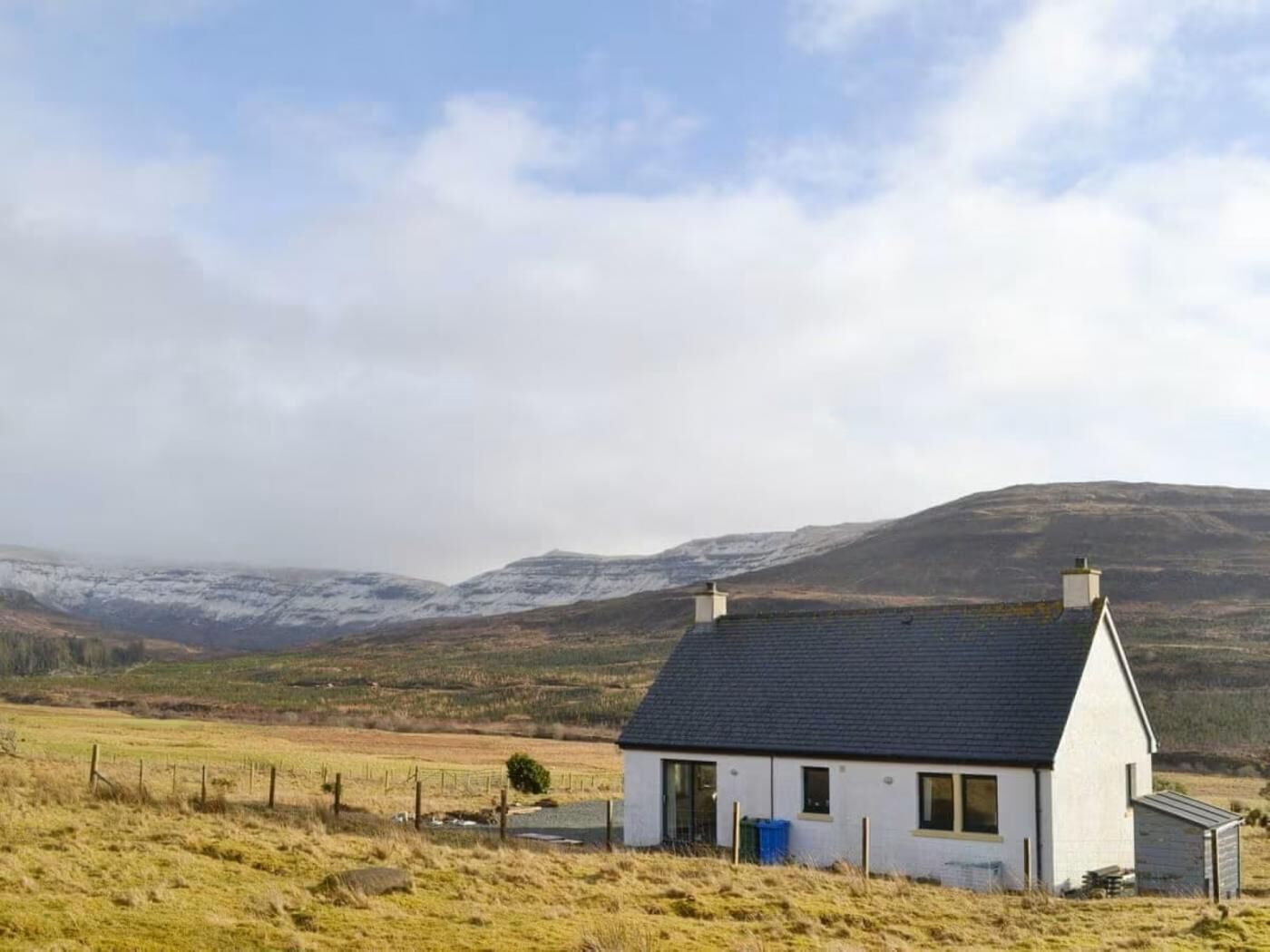 Une maison blanche avec un toit foncé, un petit garage attenant et une cour clôturée.