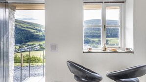 A room with a large window offering a view of a green valley and hills. There are two black chairs and a small table with a cup and saucer. - 1 Bed in Abergynolwyn (oc-p32345) (Abergynolwyn)