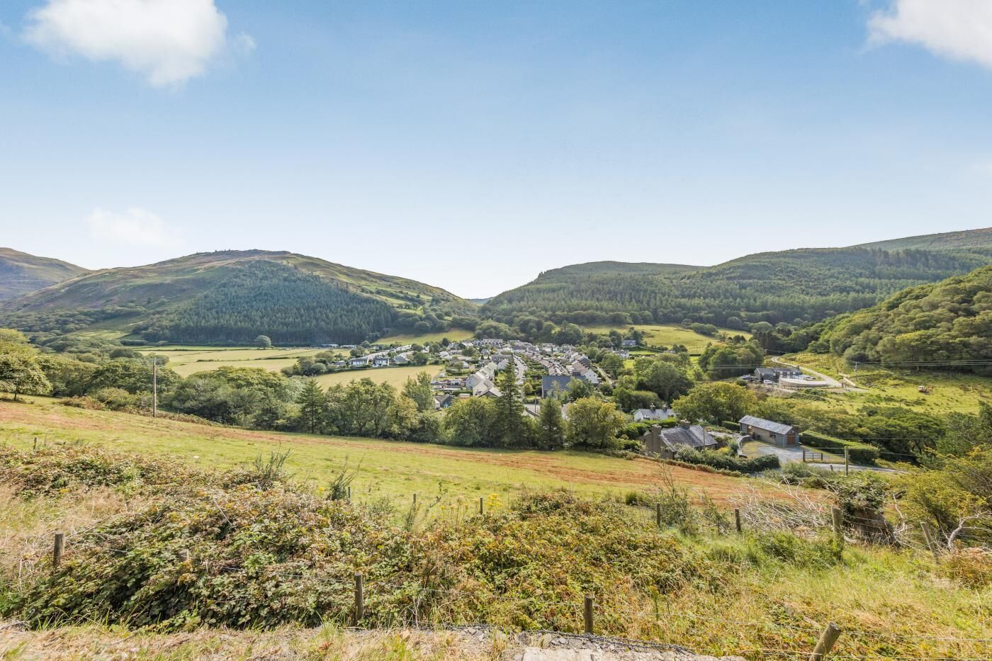 A rural village with houses and fields, surrounded by hills.