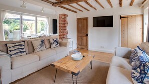 A modern living room with a wooden ceiling, a brick fireplace, and a large window overlooking a garden. - 3 Bed in Holt (oc-2150) (Holt)