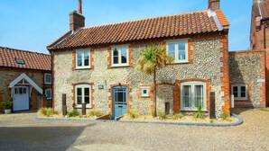 A two-story stone house with a tiled roof, multiple windows, and a small garden area. - 3 Bed in Holt (oc-2150) (Holt)