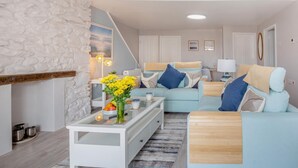 Een moderne woonkamer met een accentmuur van steen, een zithoek, een salontafel en een eethoek met een witte tafel en stoelen.
