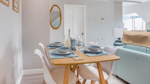Een eetruimte met een tafel voor vier personen, witte stoelen, een spiegel en een lichtblauwe bank op de achtergrond.