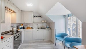 Een kleine keuken met witte kastjes, een fornuis en een eethoek met blauwe stoelen.