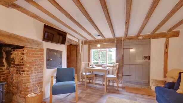 Ein gemütliches Wohnzimmer mit sichtbaren Holzbalken, einem Kamin, einem Essbereich mit Tisch und Stühlen sowie einem blauen Sofa.