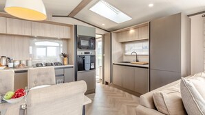 A modern kitchen with a microwave, oven, and sink, connected to a dining area with a table and chairs. - 2 Bed in Hendra Croft (oc-h32360) (Croft)