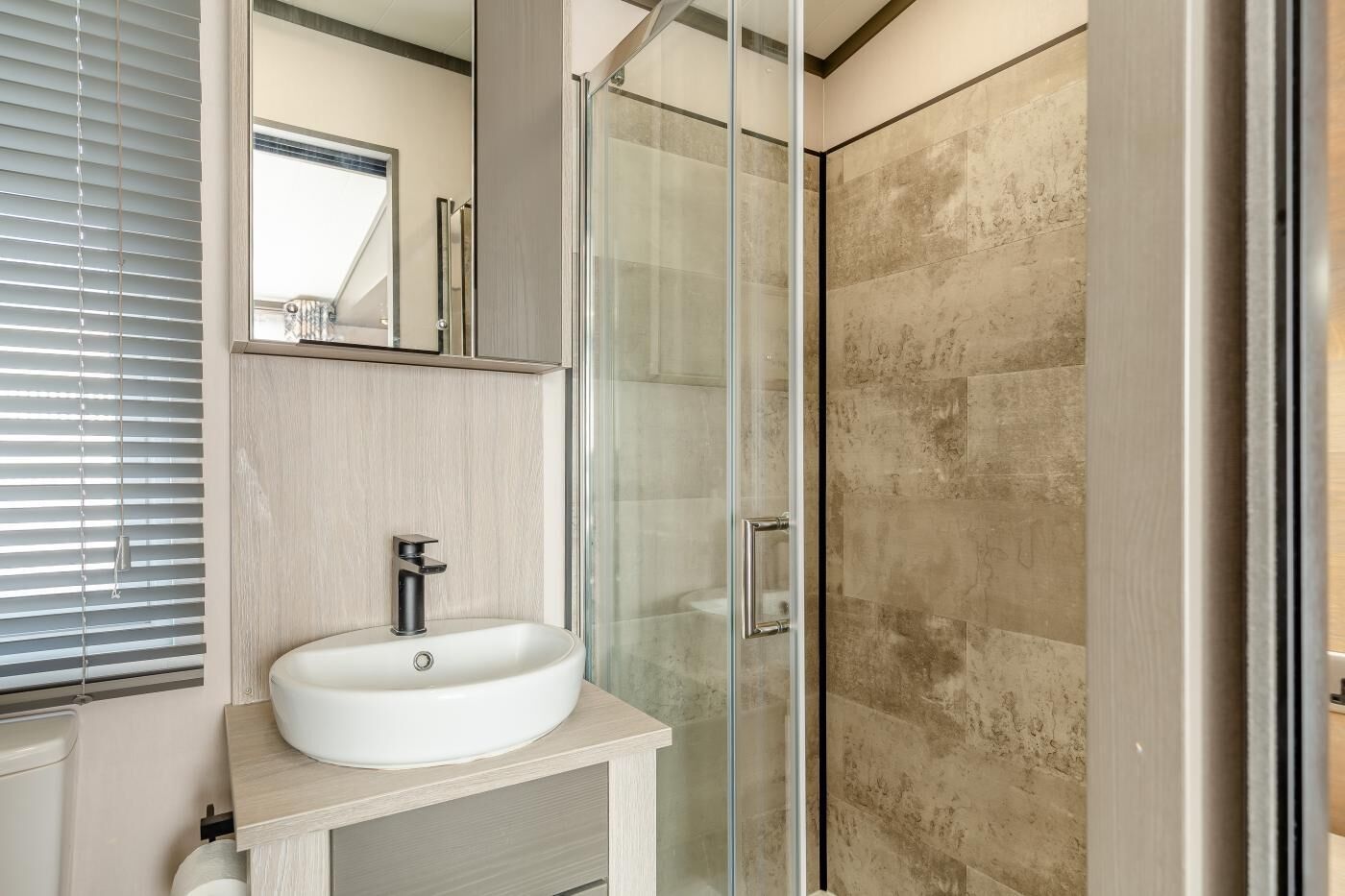 A modern bathroom with a glass-enclosed shower, a white sink, and a mirror above the sink.