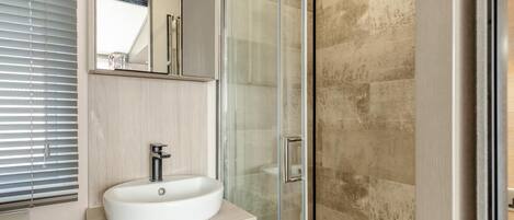A modern bathroom with a glass-enclosed shower, a white sink, and a mirror above the sink.