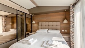 A modern hotel room with a large bed, a glass-enclosed walk-in closet, and a wooden headboard. - 2 Bed in Hendra Croft (oc-h32360) (Croft)