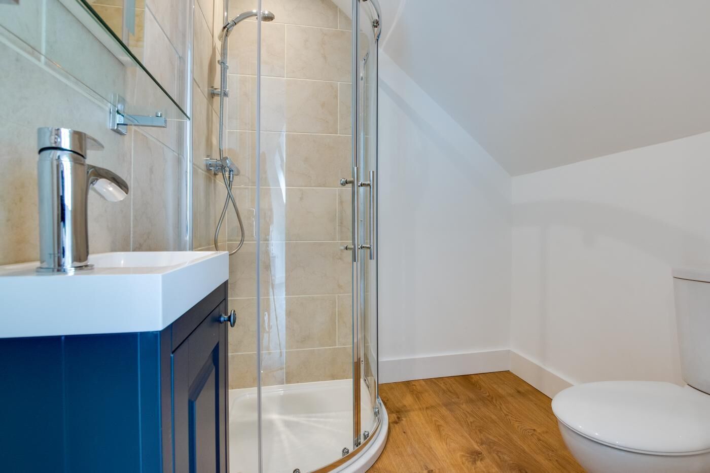 A modern bathroom with a glass shower enclosure, a white toilet, and a wooden floor.