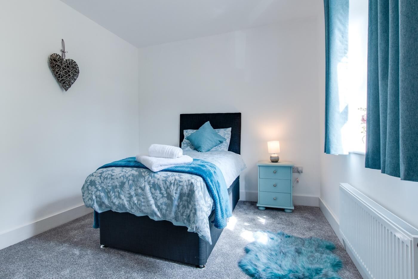 A bedroom with a bed, a nightstand, a heater, and a window with curtains.