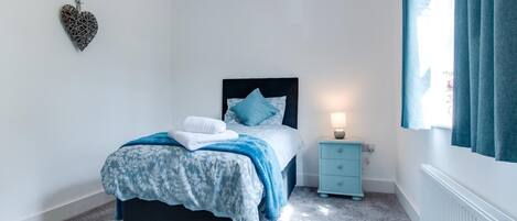 A bedroom with a bed, a nightstand, a heater, and a window with curtains.
