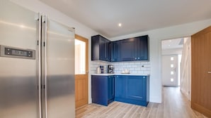 A modern kitchen with dark blue cabinets, a stainless steel refrigerator, and a tiled backsplash. - 3 Bed in Llanfynydd (oc-pw9215) (Llanfynydd)