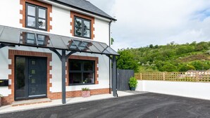 A two-story house with a covered porch, a black door, and a brick facade. - 3 Bed in Llanfynydd (oc-pw9215) (Llanfynydd)
