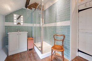 A bathroom with a shower, a sink, and a chair.