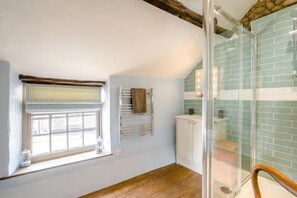 A bathroom with a shower, a window with blinds, a towel rack, and a cabinet.